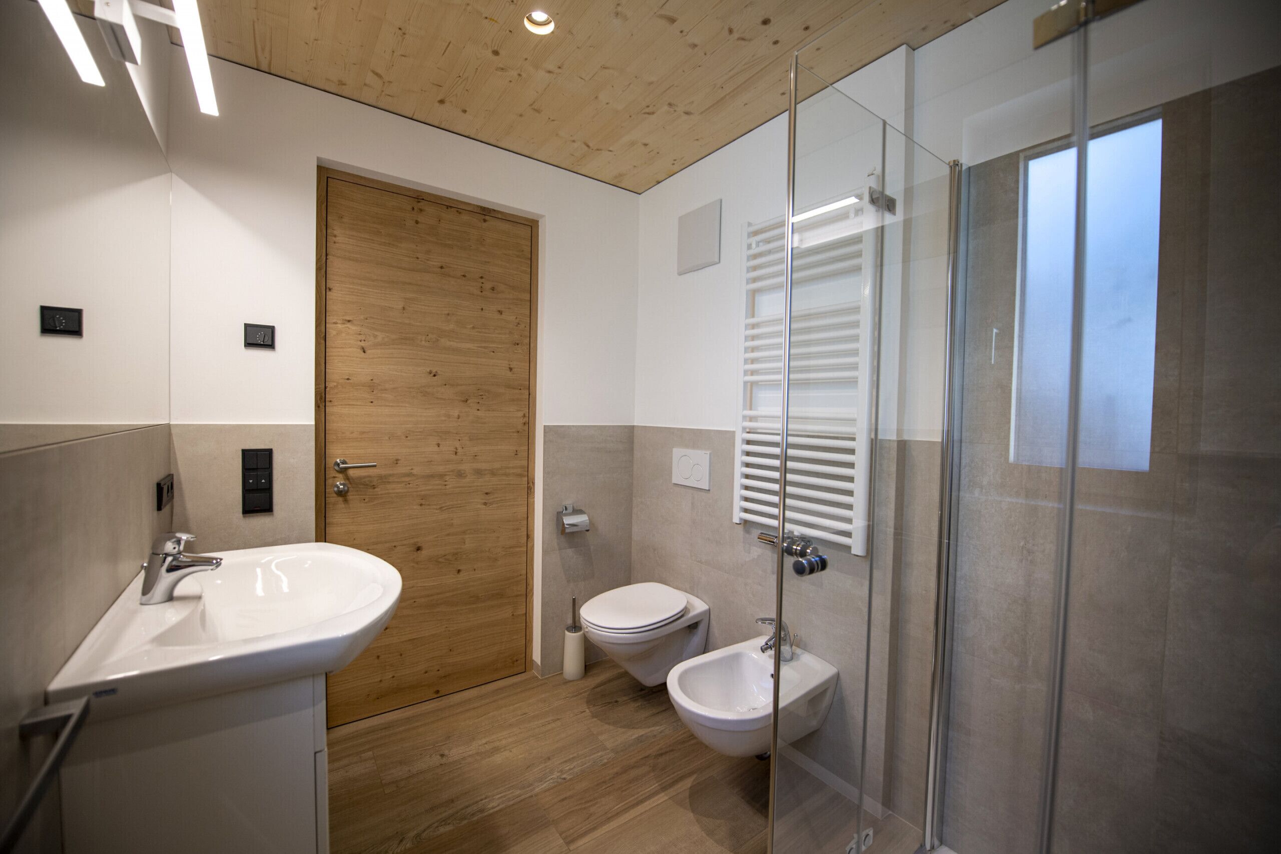 Et moderne badeværelse med en trædør, et glasbadeværelsesafskærmning, en hvid vask og en bidet.