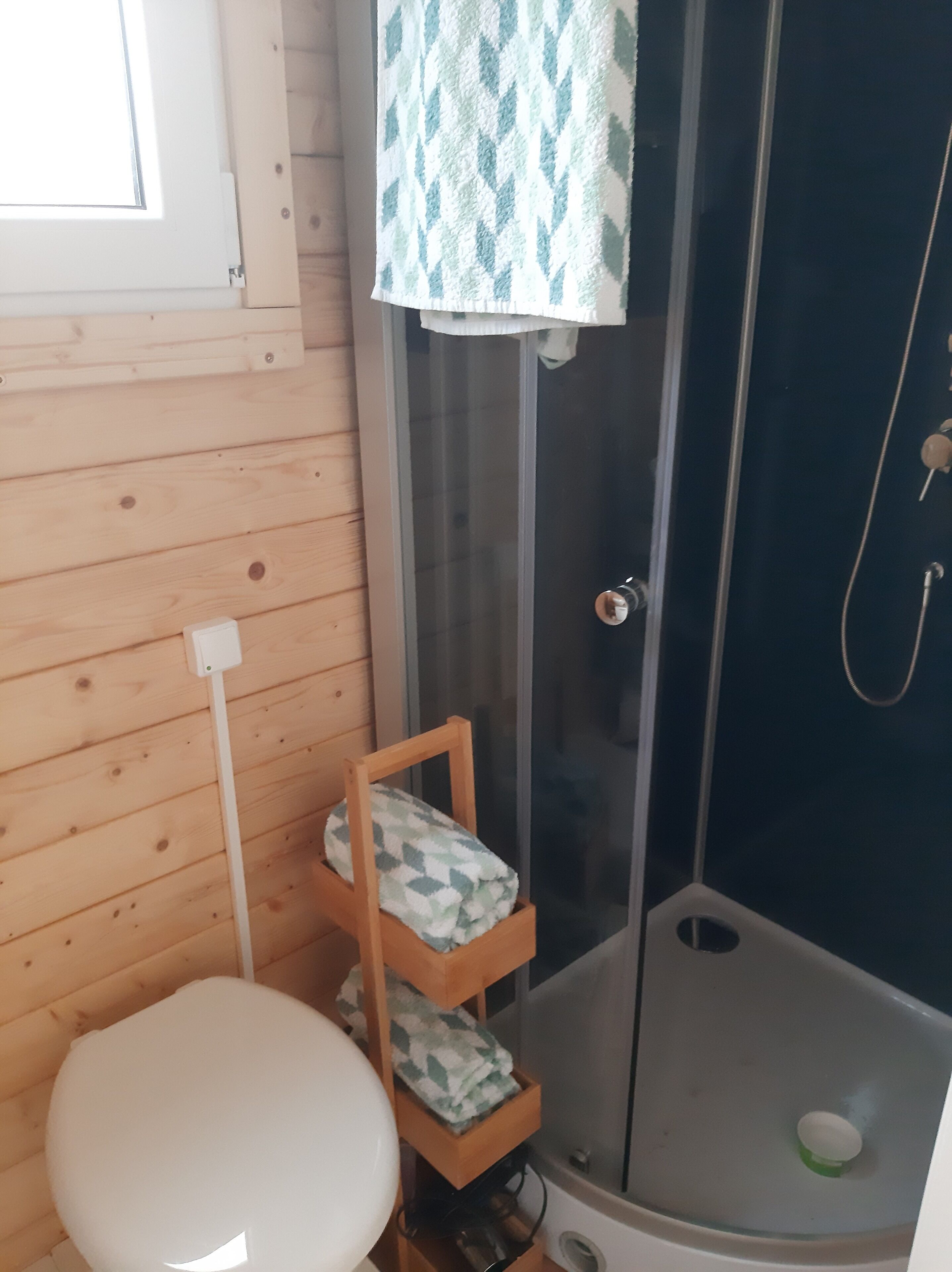 A bathroom with a shower, a toilet, and a wooden shelf with a patterned towel.