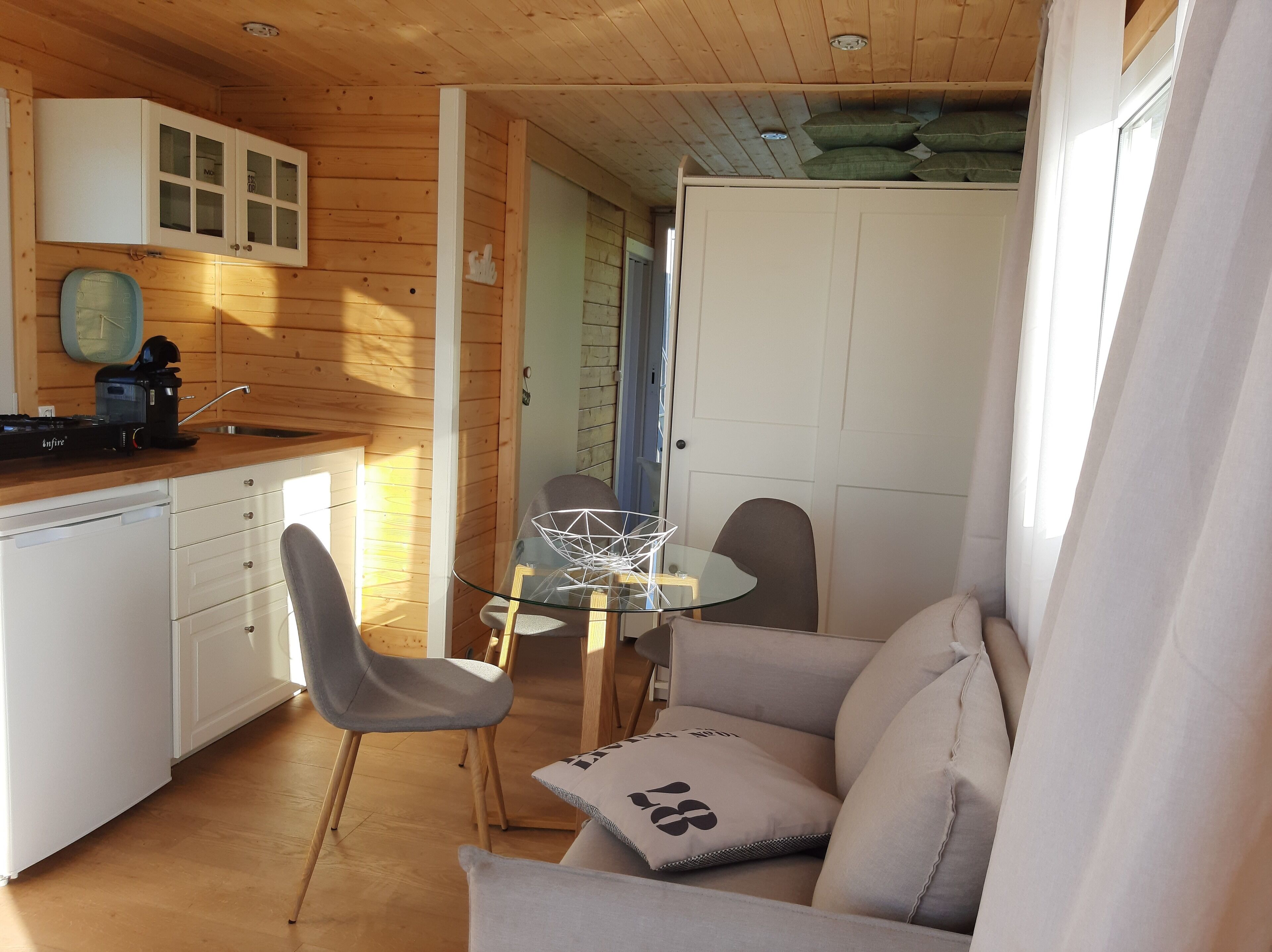A compact kitchen with wooden cabinets, a dining area with a glass table, and a sofa with cushions.