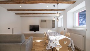 A modern dining area with a wooden ceiling, a TV mounted on the wall, and a table set for four with patterned tablecloths.