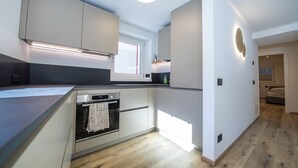 A modern kitchen with built-in appliances, a window for natural light, and a view into the adjacent bedroom.