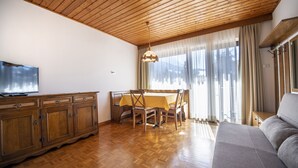 Een woonkamer met een houten plafond, een bank, een eettafel met stoelen en een tv op een houten kast.