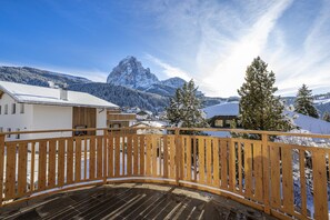 A wooden deck with a view of snow-covered houses and mountains. - Apartments Praruf 171A (Selva di Val Gardena)