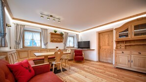 Un salón acogedor con suelo de madera, un sofá rojo, una mesa de comedor de madera con sillas, un televisor y armarios de madera.