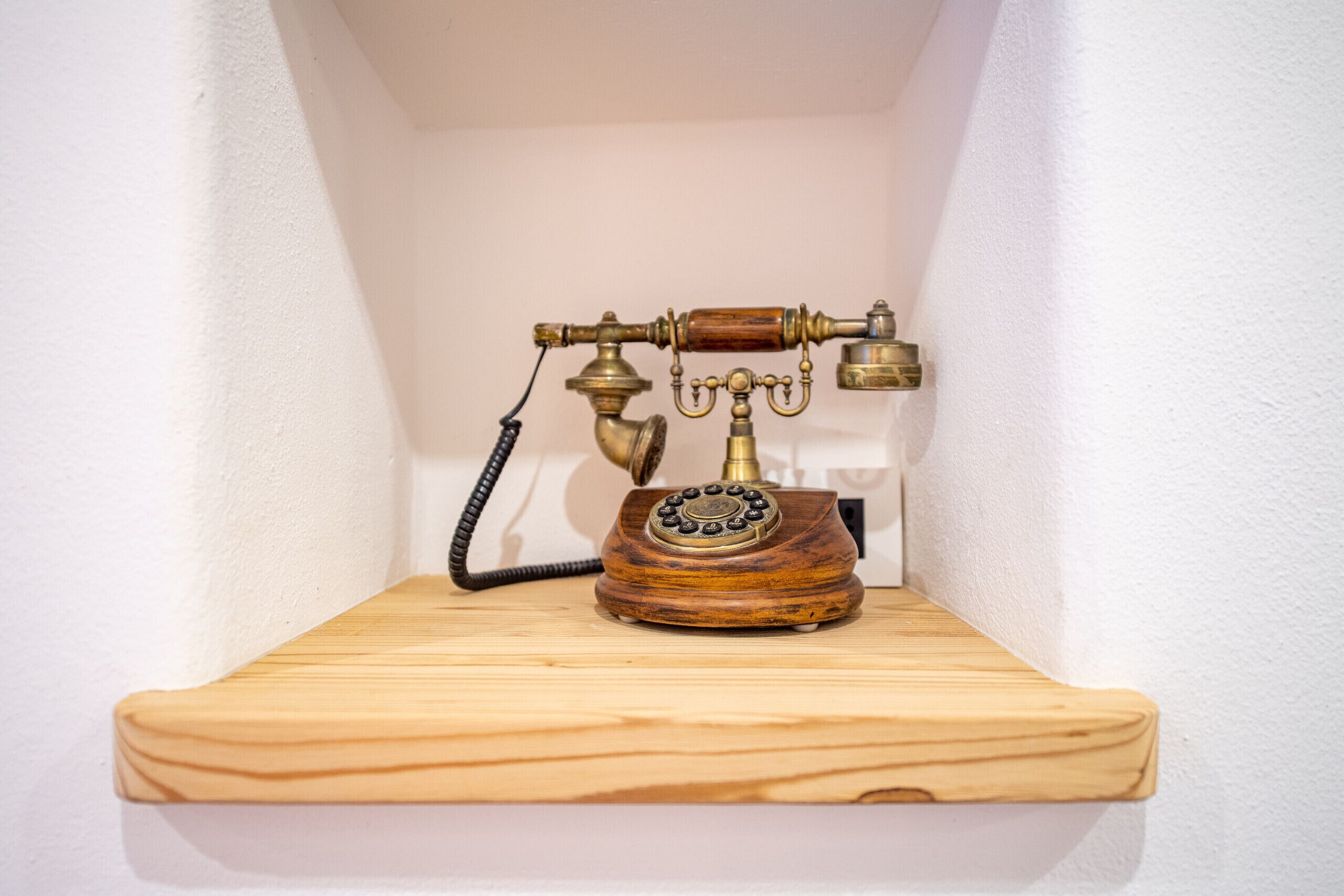 Ein altes Wählscheiben-Telefon auf einem Holzbrett vor einer weißen Wand.