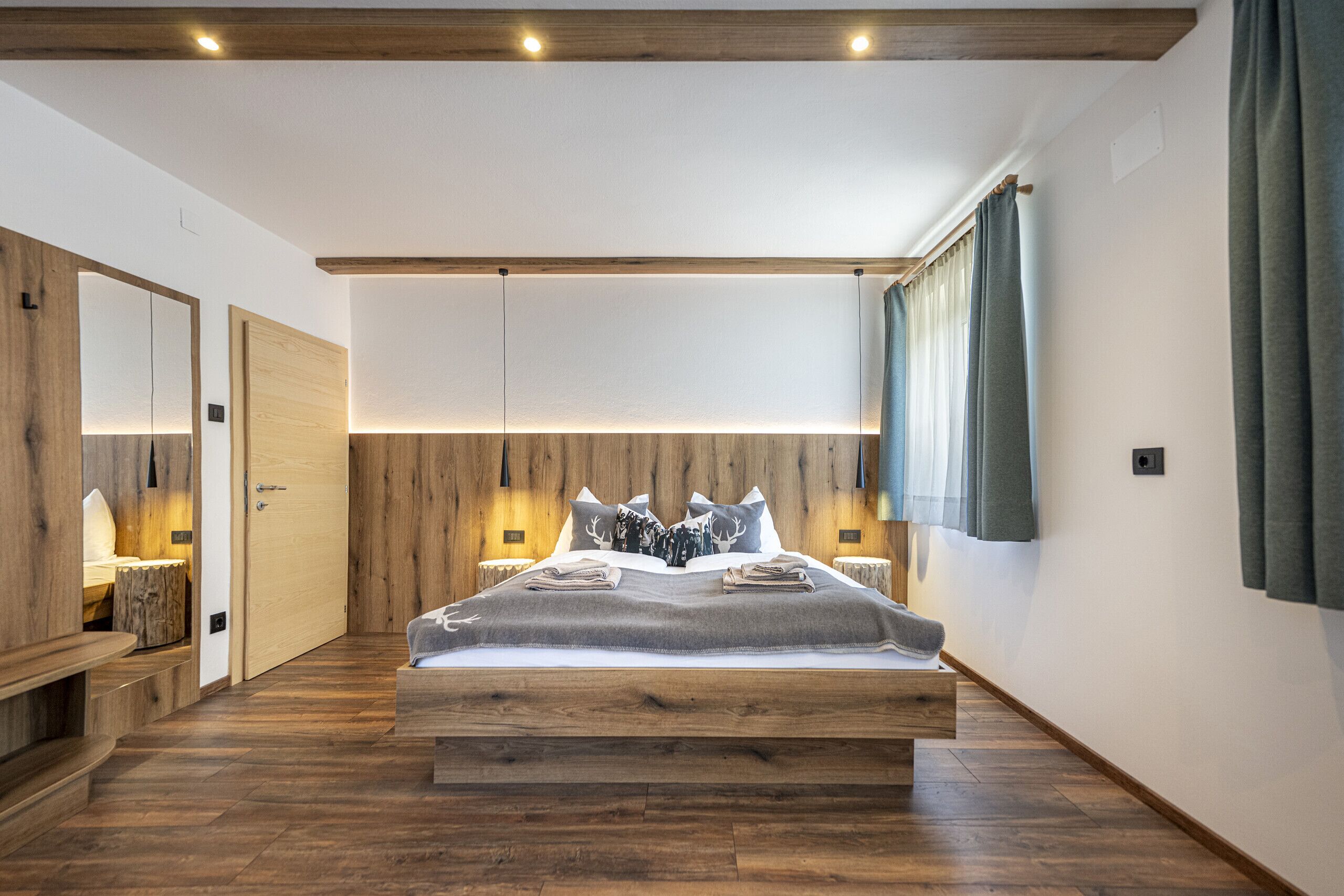 A bedroom with a wooden bed, a nightstand, a mirror, and a wooden floor.