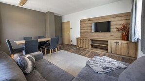 Ein modernes Wohnzimmer mit einer Couch, einem Esstisch mit Stühlen, einem flachbildfernseher an einer Holzwand und einem Kamin.