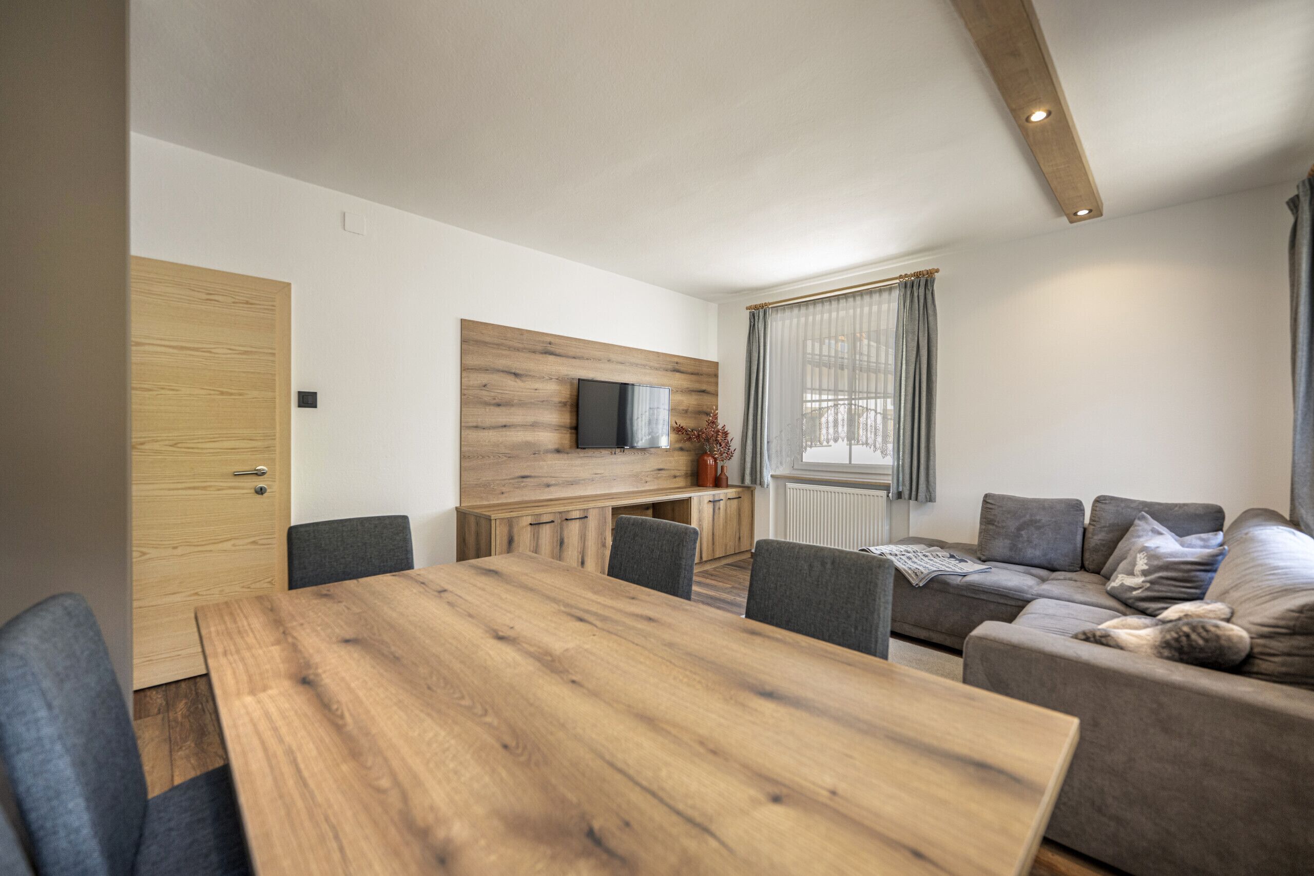 Un soggiorno moderno con un tavolo da pranzo in legno, divani grigi e TV a incasso.