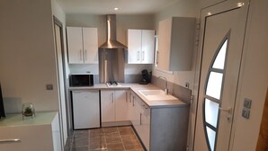 A compact kitchen with white cabinets, a stainless steel range hood, a microwave, a sink, and a refrigerator. - Country cottage (Flassans-sur-Issole)