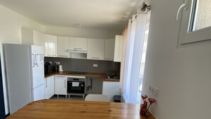 Une cuisine de taille réduite avec des meubles blancs, une table en bois et une chaise blanche.