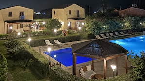 Een nachtzicht van een resort met een zwembad, ligbedden en een prieel.