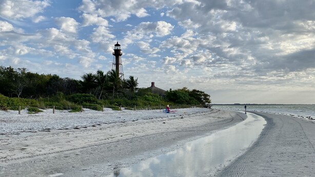 Ein Strand mit Leuchtturm, Sandstrand und blauem Himmel.