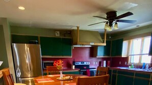 Eine moderne Küche mit Essbereich, ausgestattet mit einem runden Holztisch, Stühlen, einem Kühlschrank und einem Deckenventilator.