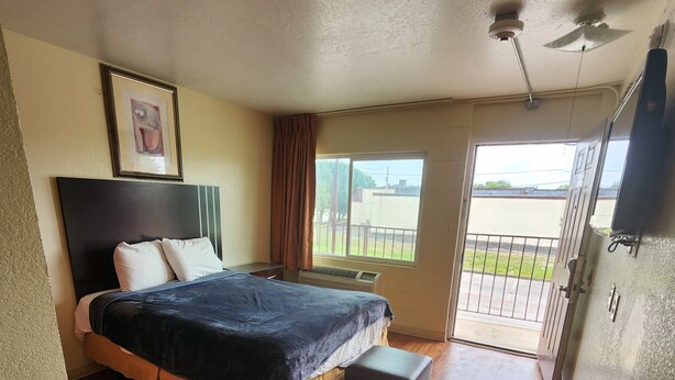 Habitación de hotel con cama, una mesita, una silla, ventilador de techo y ventana con vistas al exterior.