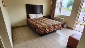 Una habitación de hotel con una cama, una ventana con cortinas, piso de baldosas y una pequeña mesa.