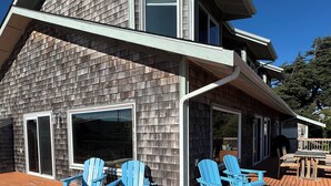 A two-story house with a deck, blue Adirondack chairs, and a large window.