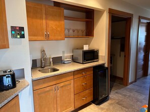 A compact kitchen with wooden cabinets, a stainless steel sink, a microwave, a toaster, and a refrigerator. - LOW TIDE JULY OPENINGS! Beach house getaway RARE AVAILABILITY! PACK YOUR BAGS! (Pacific Beach)