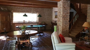 Een gezellige woonkamer met een stenen open haard, een eetgedeelte met een ronde tafel en stoelen, en een trap die naar een bovenverdieping leidt.