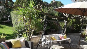 Een terras met rieten meubels, een schommelstoel en een stenen vloer.
