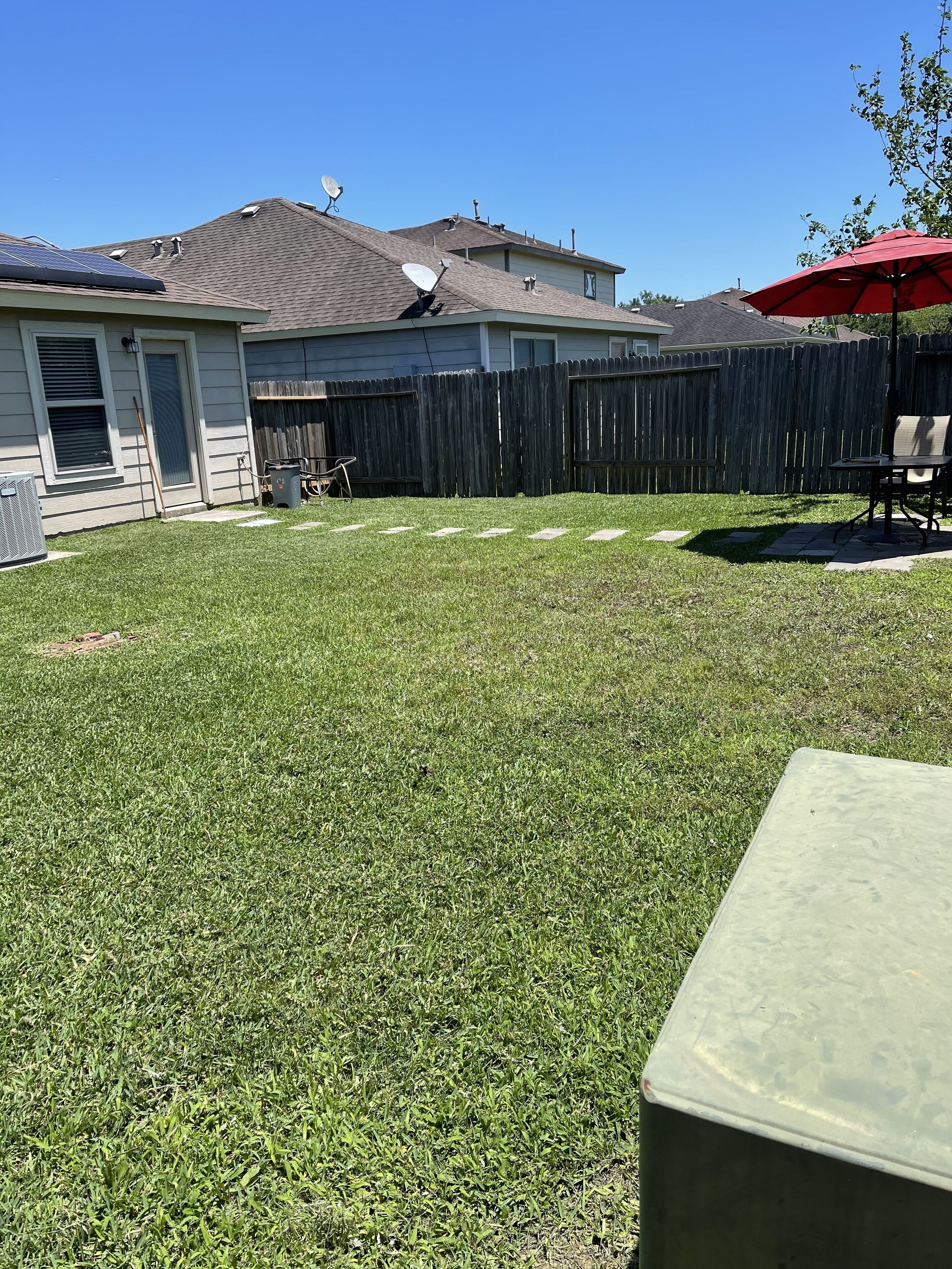 Un jardin avec une pelouse, une clôture en bois et un espace patio comprenant une table et des chaises.