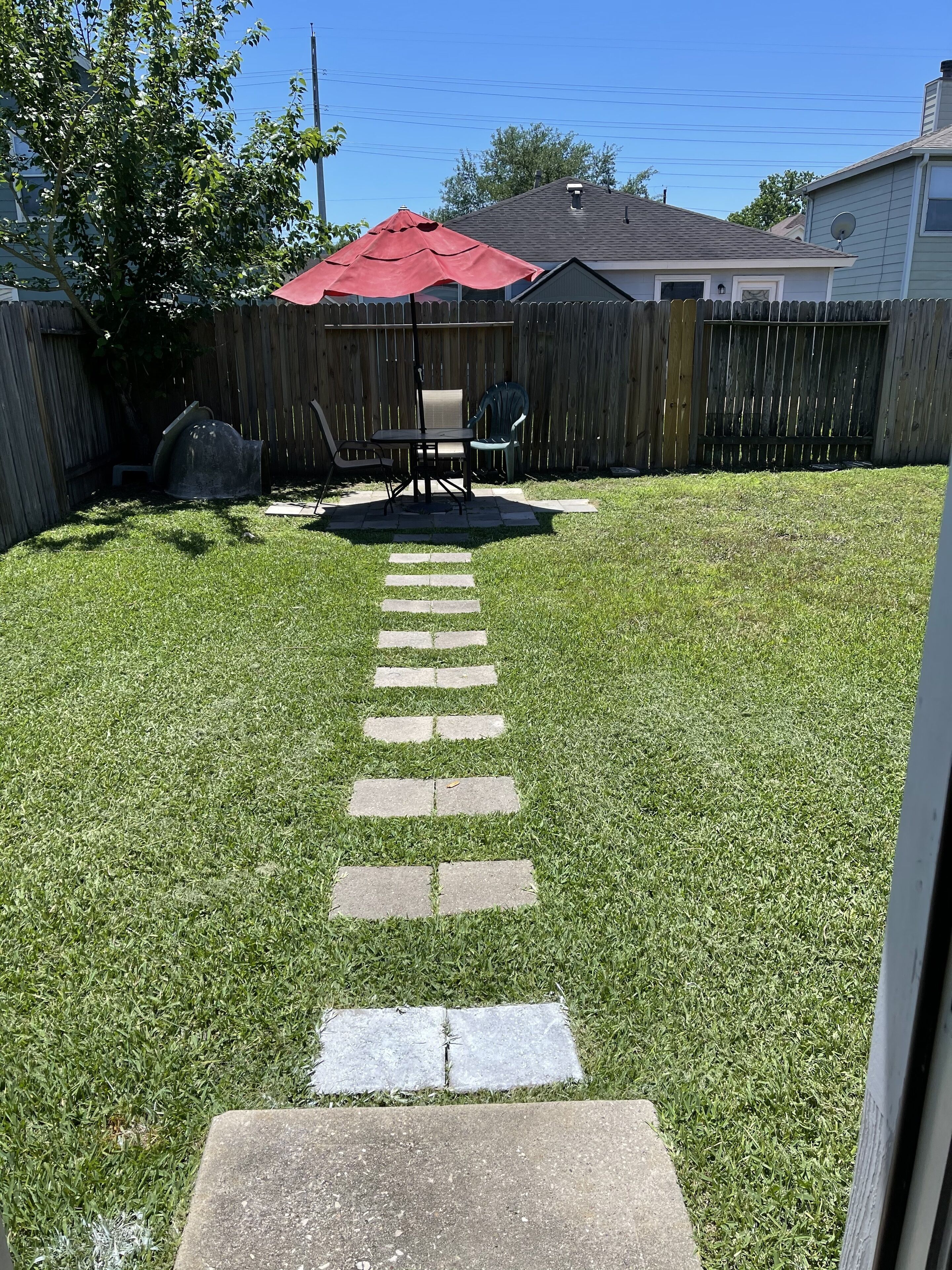 Een achtertuin met een pad van stenen dat leidt naar een terras met een tafel en stoelen.
