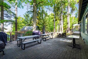 Un patio al aire libre con mesas de picnic y una parrilla, rodeado de árboles altos.