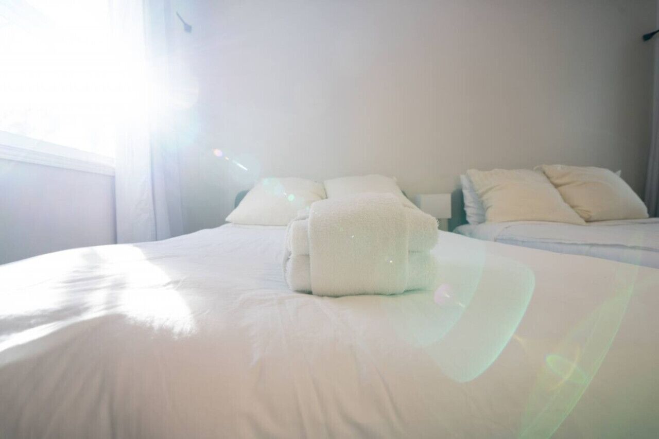 Habitación de hotel con dos camas, ropa de cama blanca y un ventanal que proporciona luz natural.
