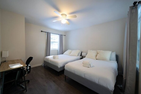A hotel room with two beds, a desk, and a ceiling fan.