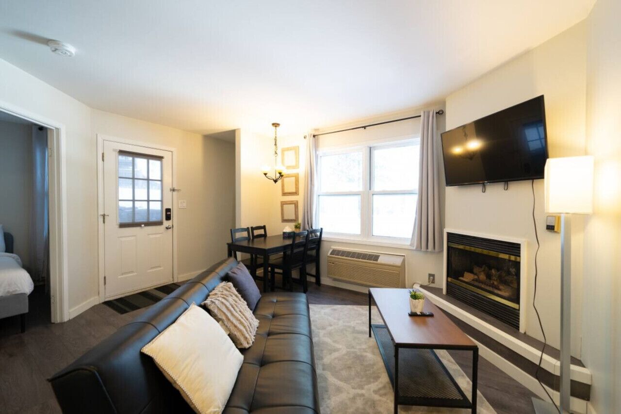 A living room with a sofa, a dining table, chairs, a fireplace, a TV, and a window.