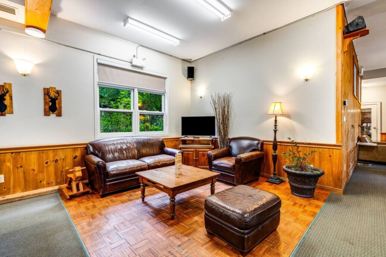 Una sala de estar con piso de madera, sofás de cuero, una mesa de centro, un televisor y un ventanal con vista a follaje.