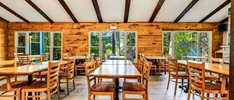 Une cabane en bois dotée de plusieurs tables et chaises, de grandes fenêtres et d’un ventilateur de plafond.