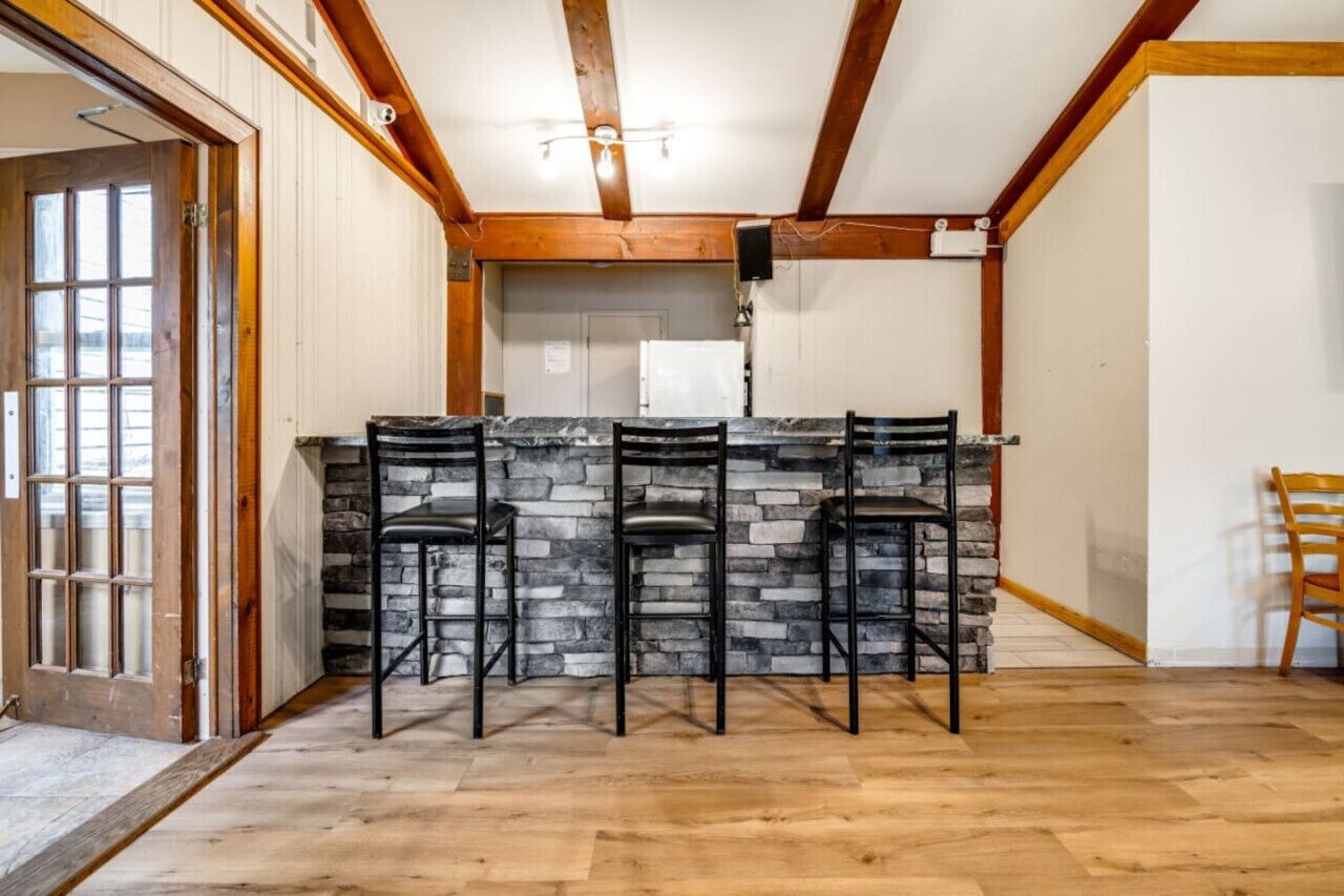 A kitchen with a stone countertop, three bar stools, wooden beams on the ceiling, and a door with glass panels.