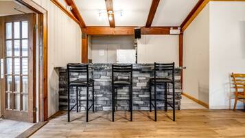 A kitchen with a stone countertop, three bar stools, wooden beams on the ceiling, and a door with glass panels.