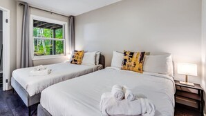 A hotel room with two beds, a window with a view of greenery, and a bedside table with a lamp. - Rare Muskoka Chalet Suite - B8 (Dwight)
