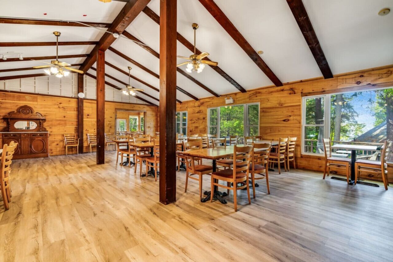 Un vaste espace dédié à la salle à manger, avec des tables et des chaises en bois, de grandes fenêtres et des poutres apparentes.