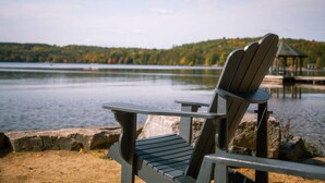 Une chaise Adirondack est placée face à un lac paisible, avec une colline boisée en arrière-plan.
