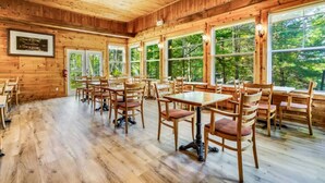 Un intérieur en bois avec des tables et des chaises, de grandes fenêtres et un ventilateur de plafond.