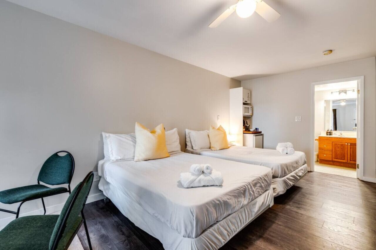 Une chambre d’hôtel avec deux lits, une chaise, une petite table et une salle de bain visible à travers une porte ouverte.