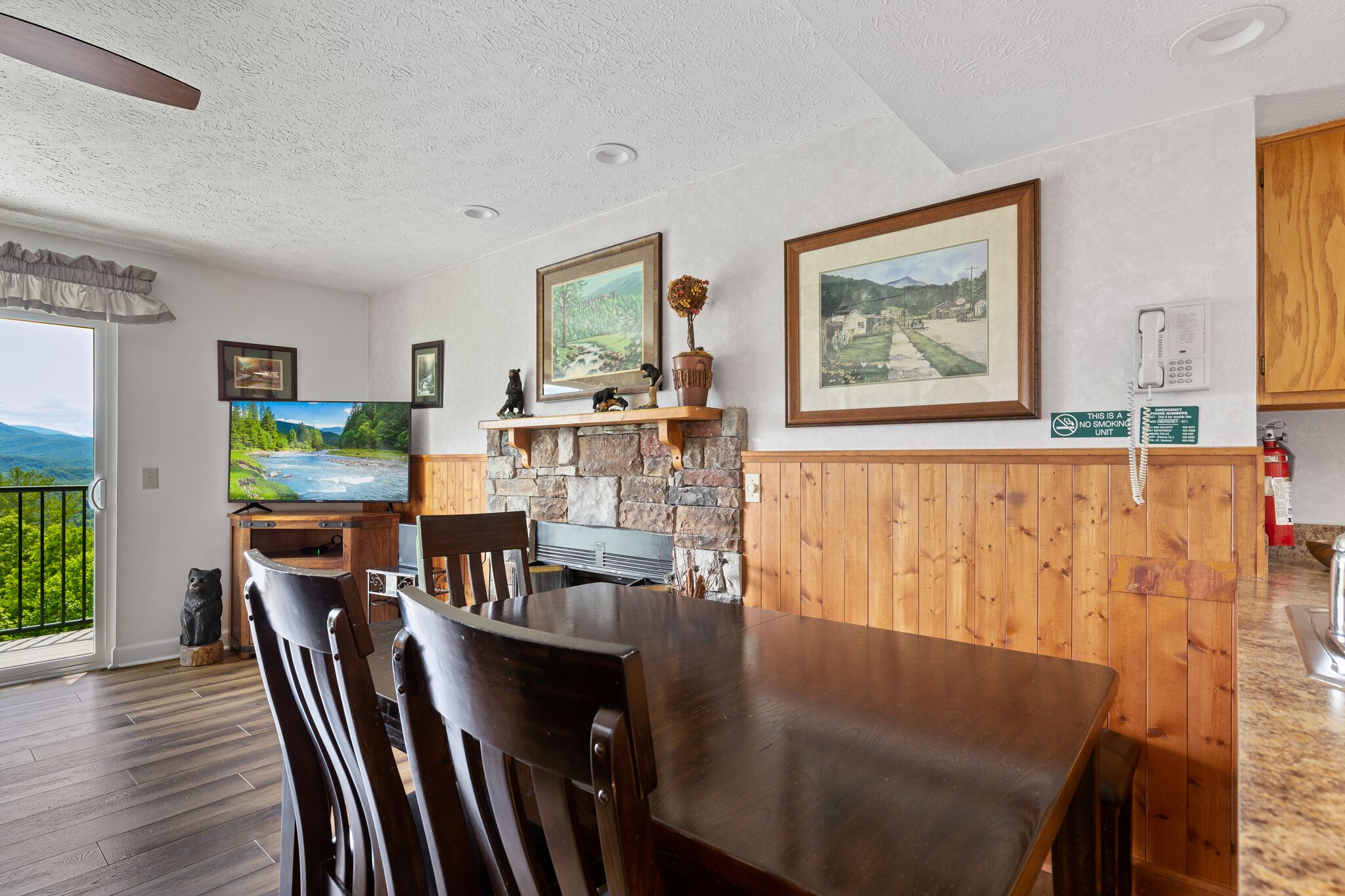 A modern kitchen with a stone wall, wooden cabinets, and a large flat-screen TV.