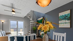 Un salon moderne avec une table à manger en bois, des chaises blanches, un canapé bleu et un escalier menant à l’étage supérieur.