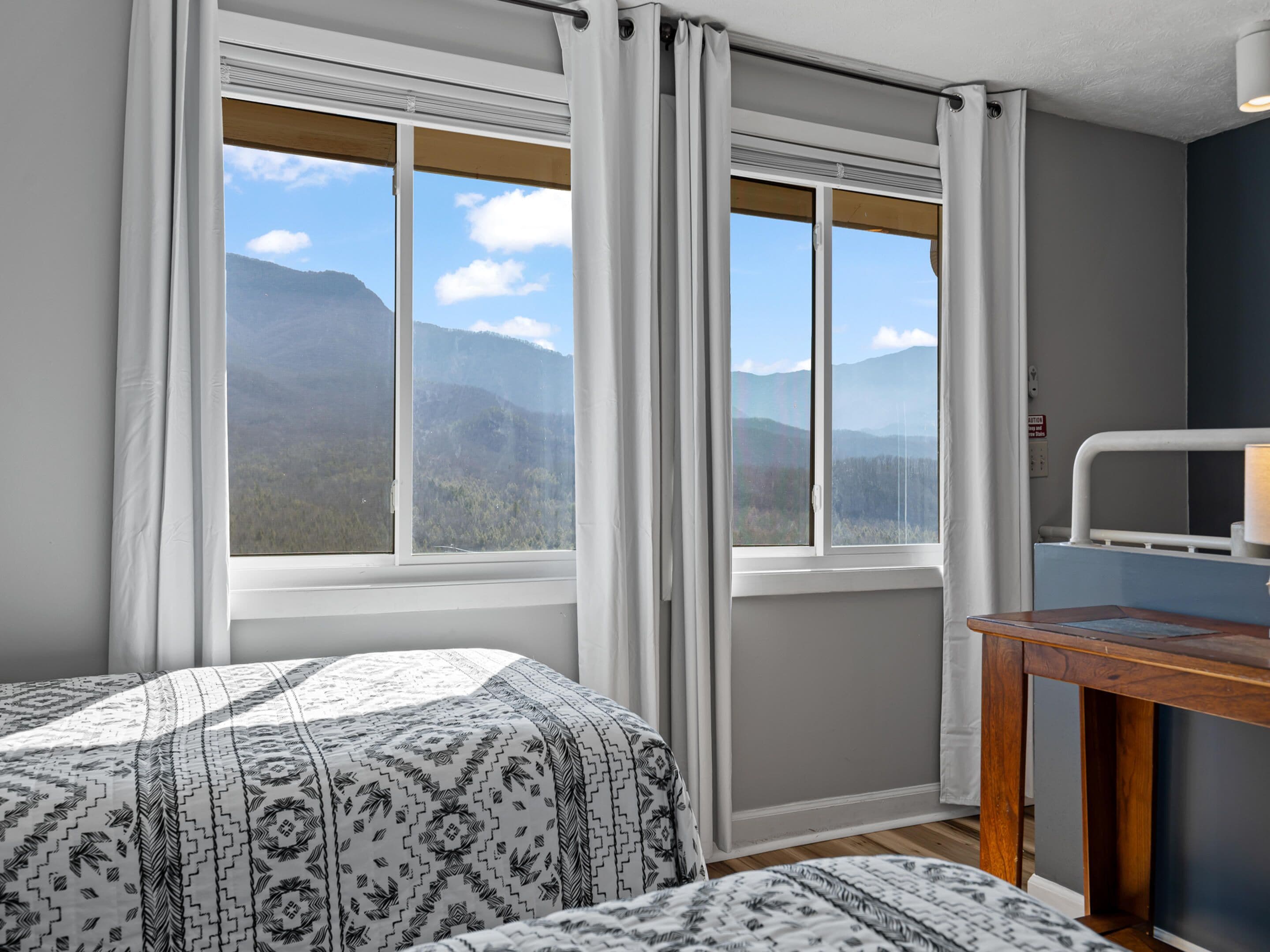 Un dormitorio con dos camas, una mesa de madera y vistas a las montañas a través de amplios ventanales.