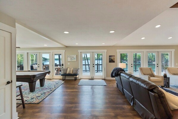 A spacious living room with a pool table, comfortable seating, and large windows.