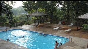 An outdoor swimming pool with a wooden deck, lounge chairs, and a gazebo. - Modern treehouse in the woods near SDC! (Reeds Spring)