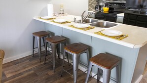 A kitchen with a central island, four stools, a sink, and a stove. - Modern treehouse in the woods near SDC! (Reeds Spring)
