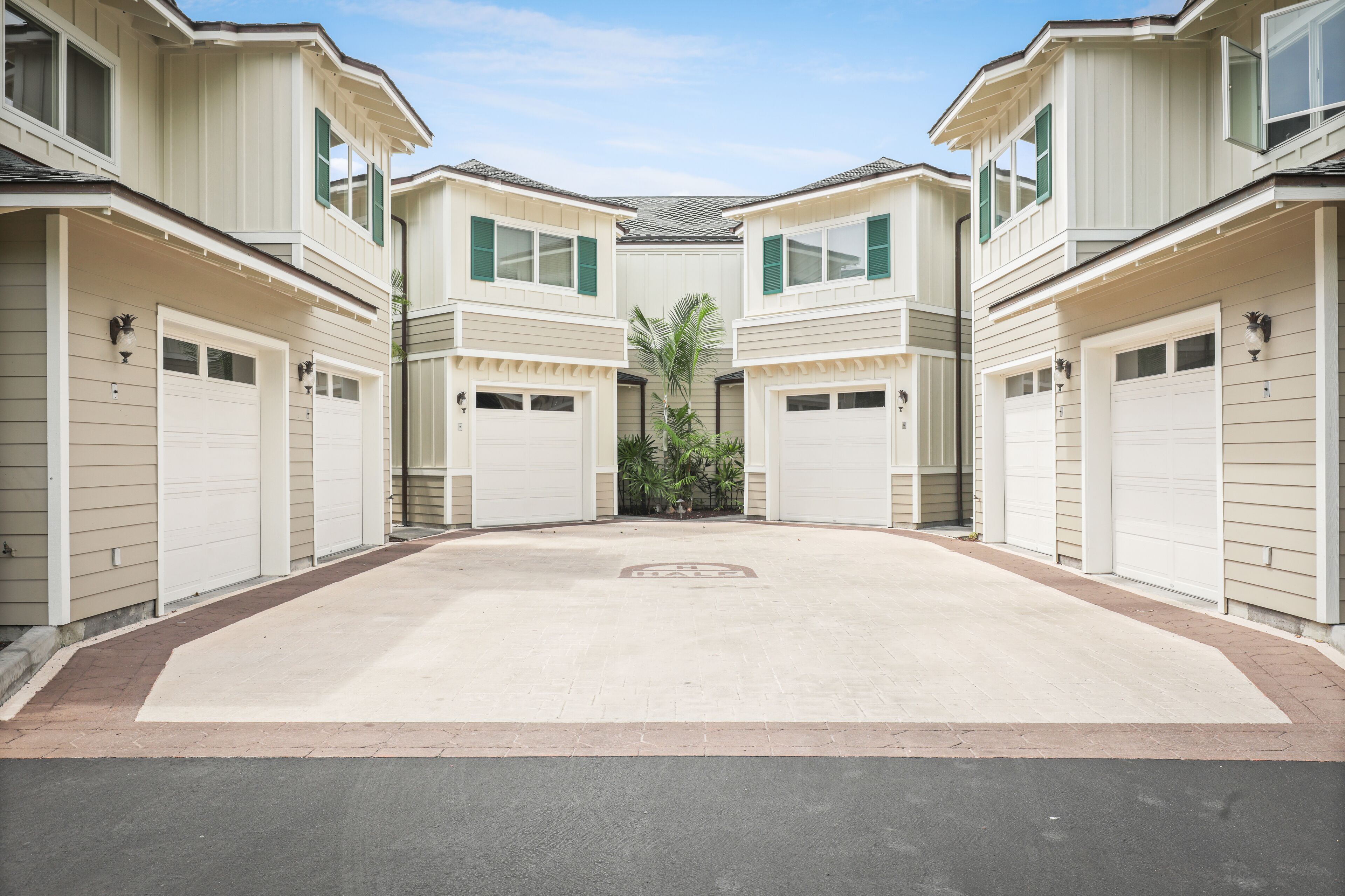 A symmetrical residential building with a central driveway, garage doors, and a palm tree in the middle.