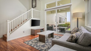 Un salon avec un escalier, un téléviseur à écran plat, un canapé et un coin repas comprenant une table et des chaises.