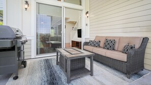 Un espace patio aménagé avec un barbecue, un canapé en osier et une porte vitrée donnant accès à un niveau supérieur.
