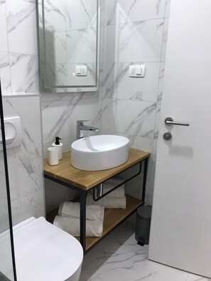 A modern bathroom with a marble backsplash, a white sink on a wooden vanity, a mirror, and a toilet.