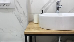 Ein Badezimmer mit einer weißen Toilette, einem weißen Waschbecken mit schwarzem Wasserhahn und einer Holzausstattung mit Marmor-Spritzschutz.