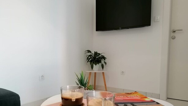 Ein modernes Wohnzimmer mit einem runden weißen Tisch, auf dem zwei Kaffeetassen, ein kleines Topfpflänzchen und ein Buch stehen.